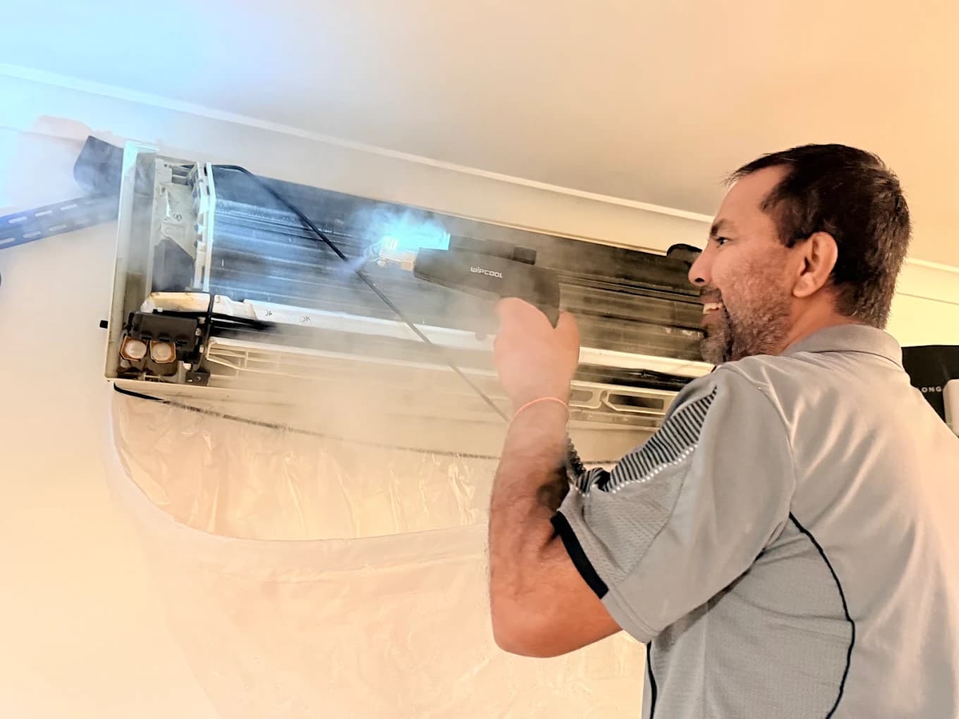 Steam cleaning a split-system air conditioner, coils exposed with visible steam